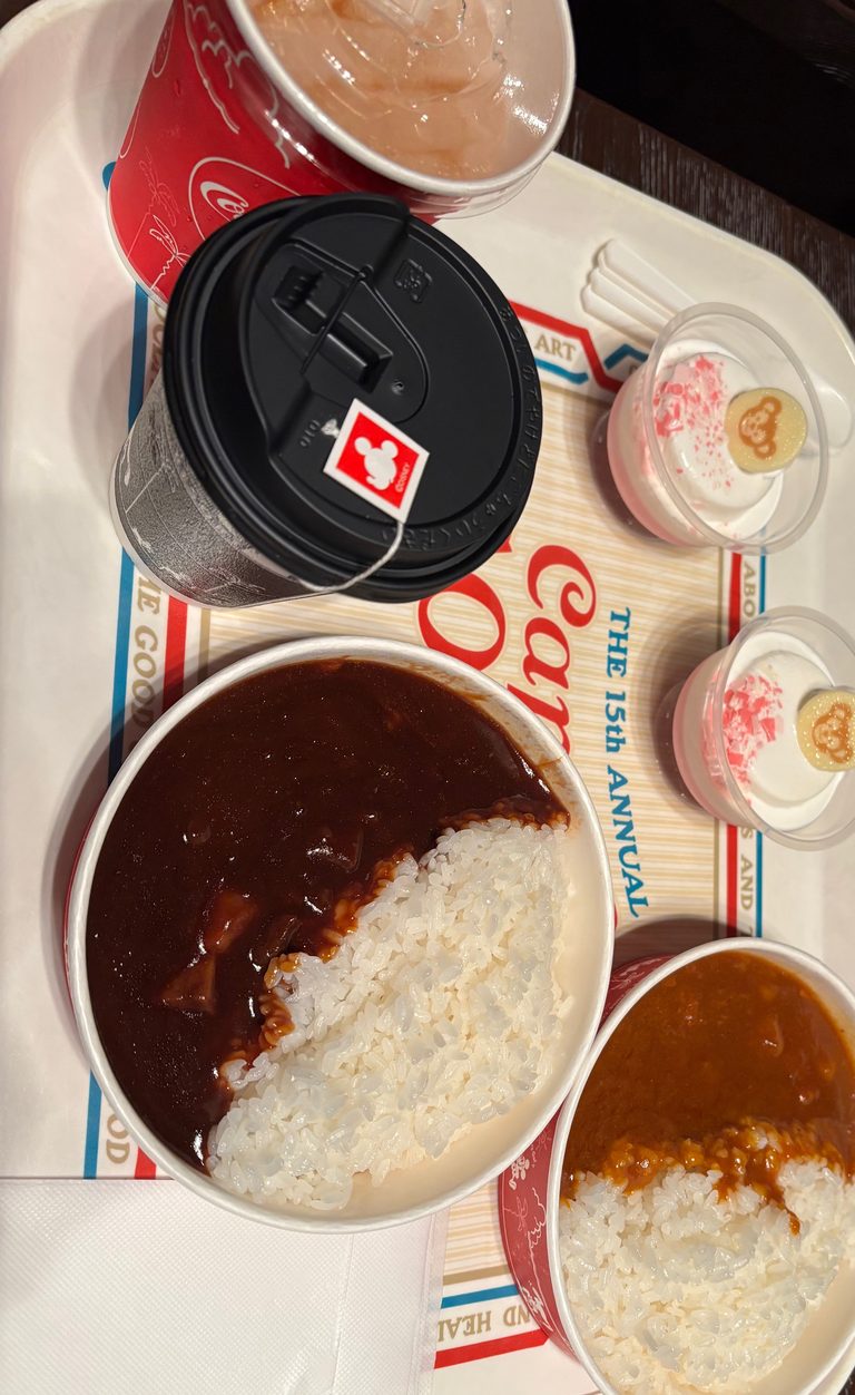 ケープコッド・クックオフのトレイに乗せた2種類のカレーとドリンク、ダッフィーの飾りが付いたデザート2つ